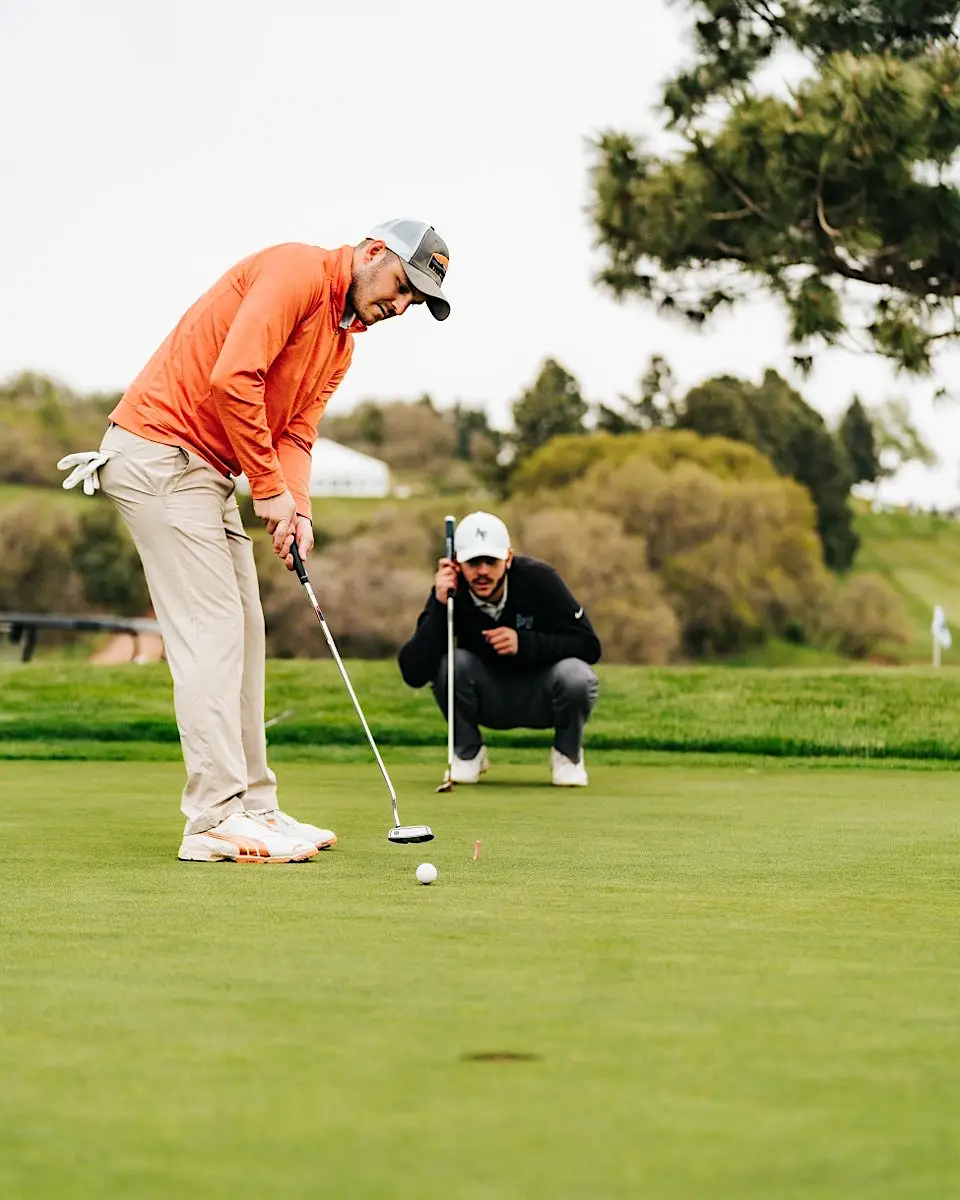 Jacob putting on a golf green with another golfer behind him watching
