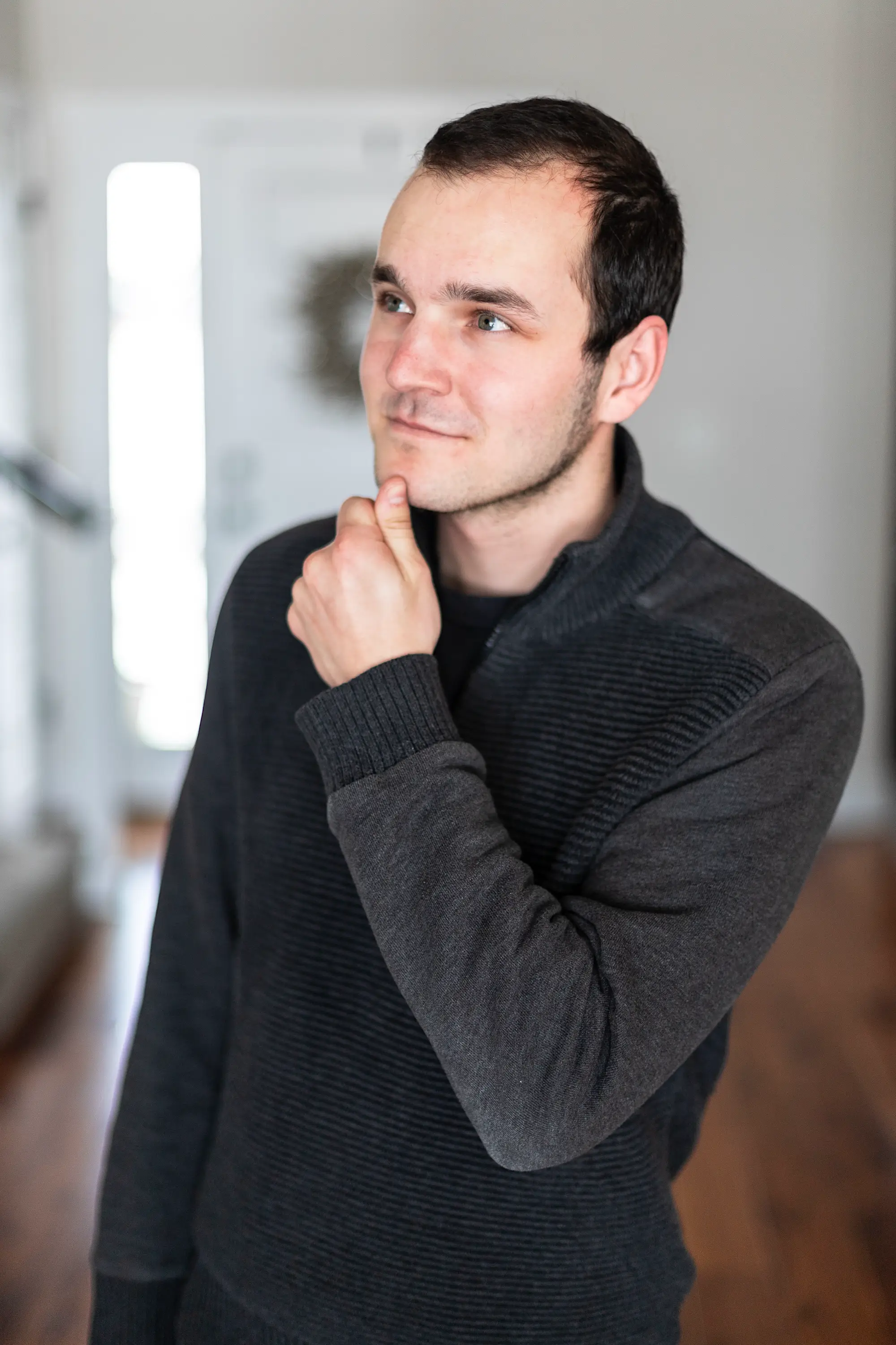 Jacob with his hand to his chin wearing a sweater looking off to the right in a house