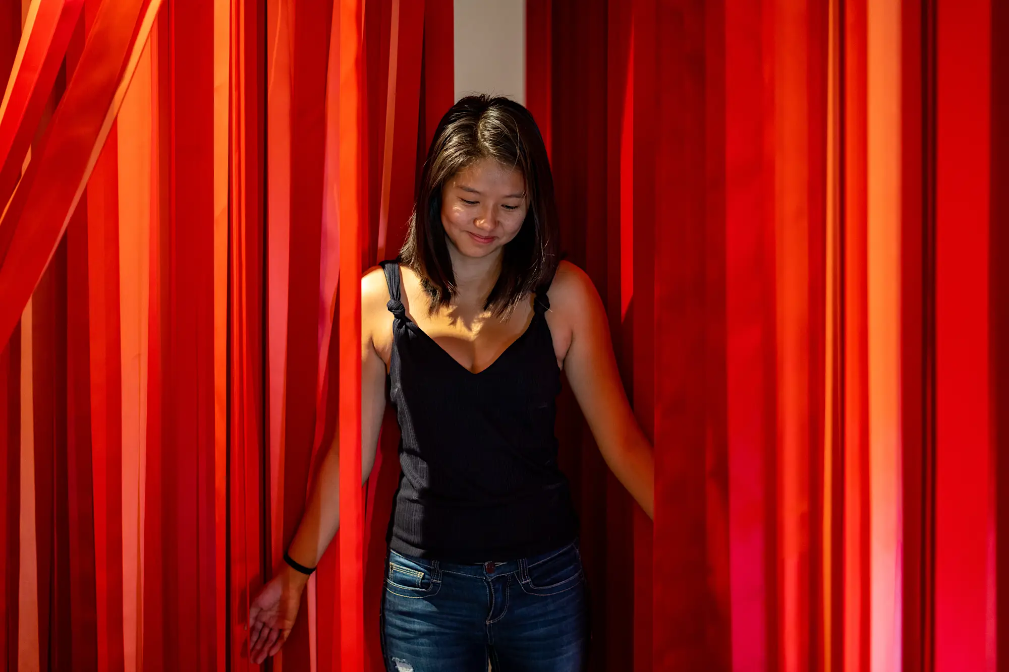 Woman walking among a sea of red ribbons wearing a black top and blue jeans