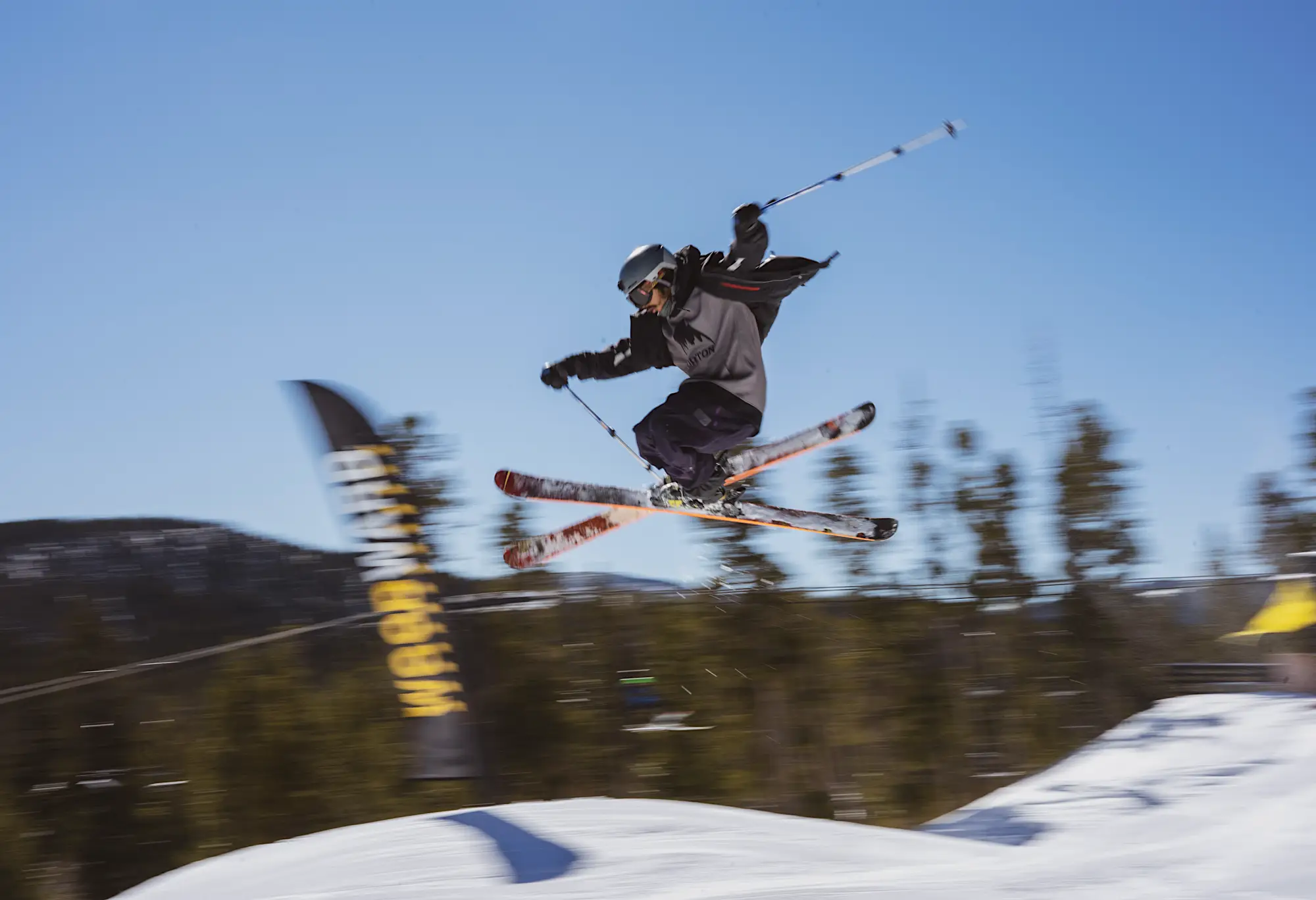 Man skiing off of a jump in the air against a blue sky and green trees