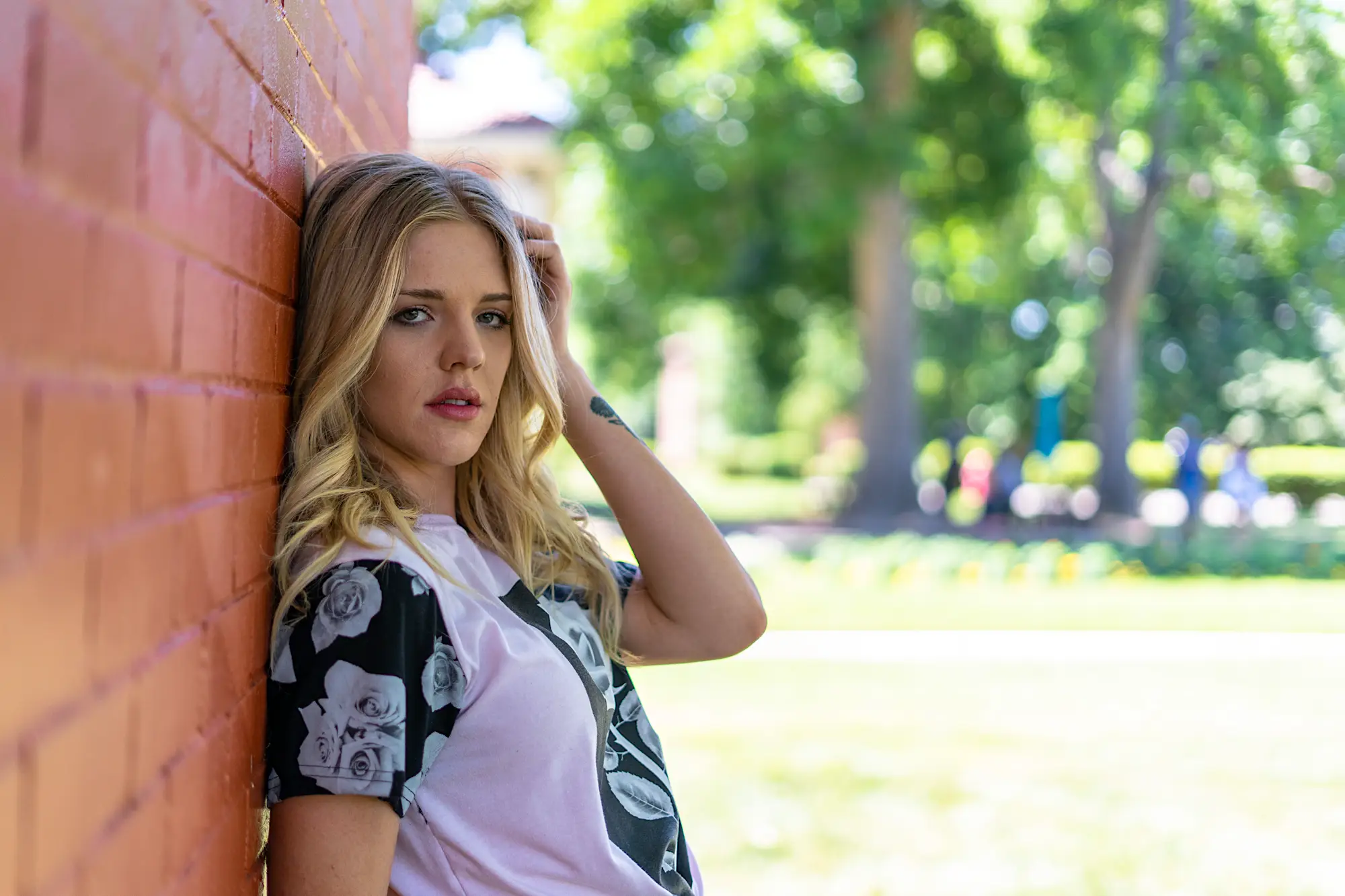 Woman leaning up against a brick wall with her hand on her head looking at the camera