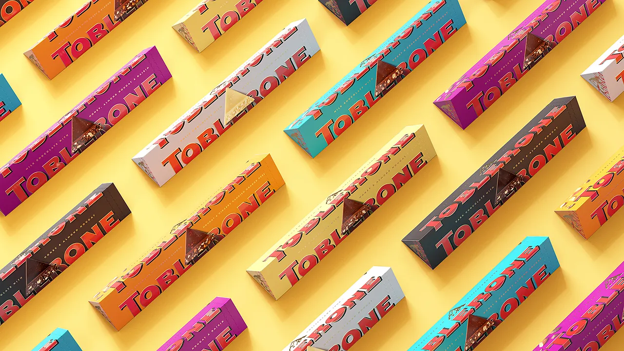 Verschiedene Packungen Toblerone in unterschiedlichen Farben auf gelbem Grund