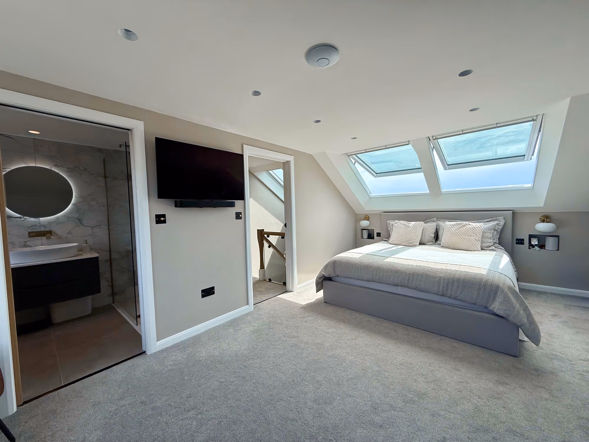 A tidy bedroom with a large bed, skylights, and an adjacent bathroom.