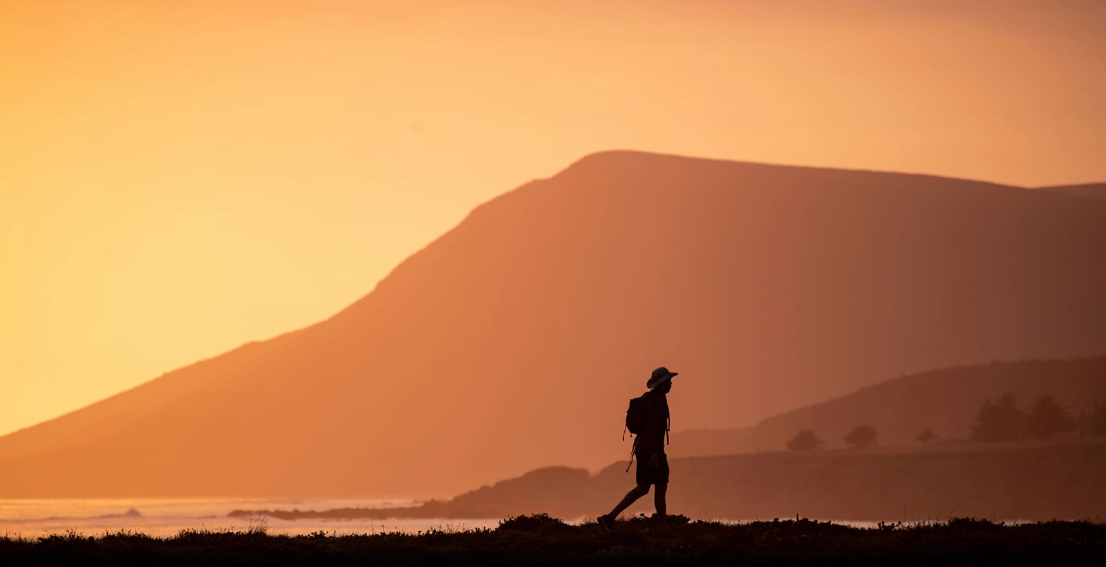 A young solo traveller with a backpack walking under a sunset sky.