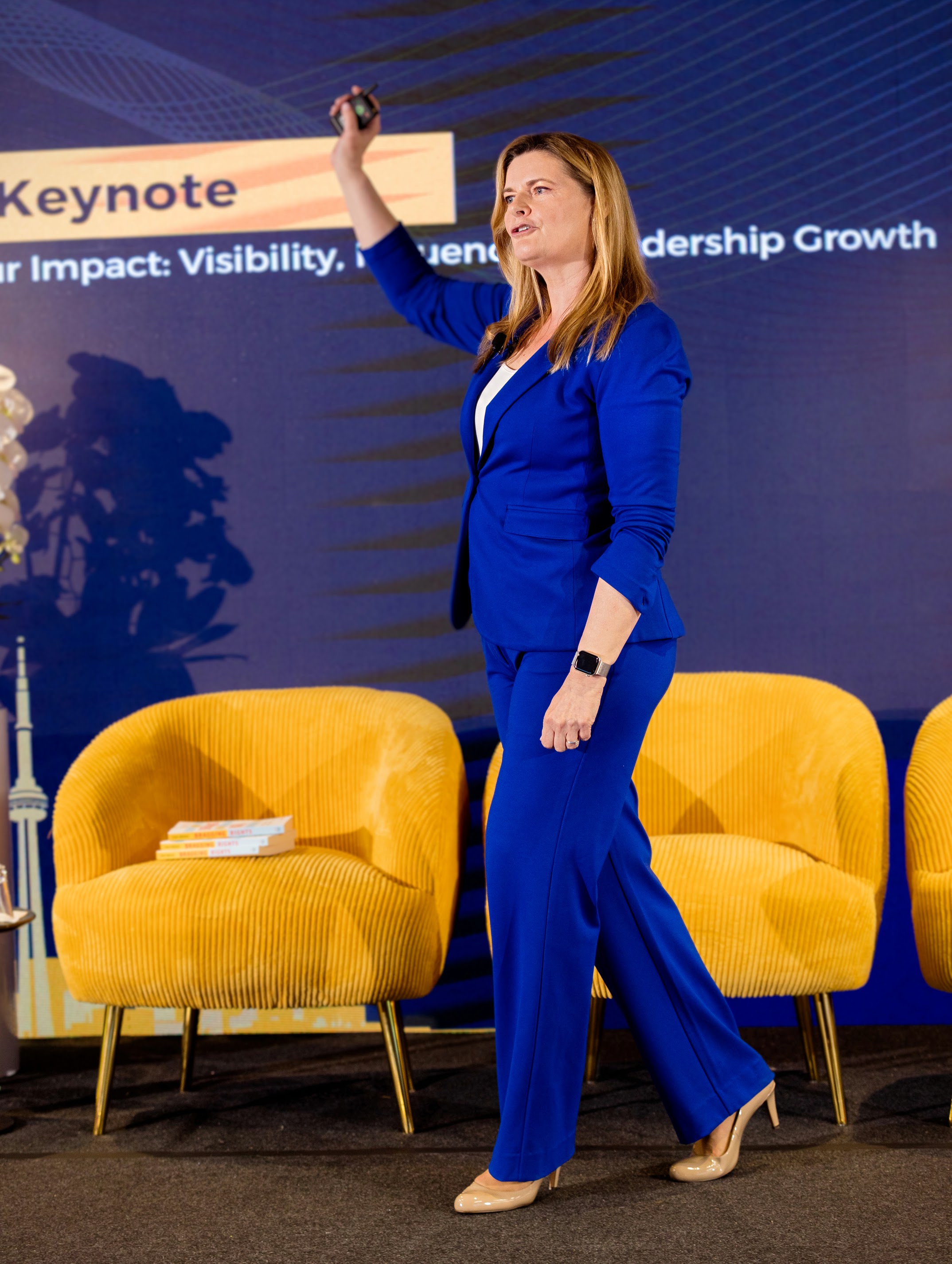 Lisa Bragg on stage wearing a blue suit. Her arm is raised. 