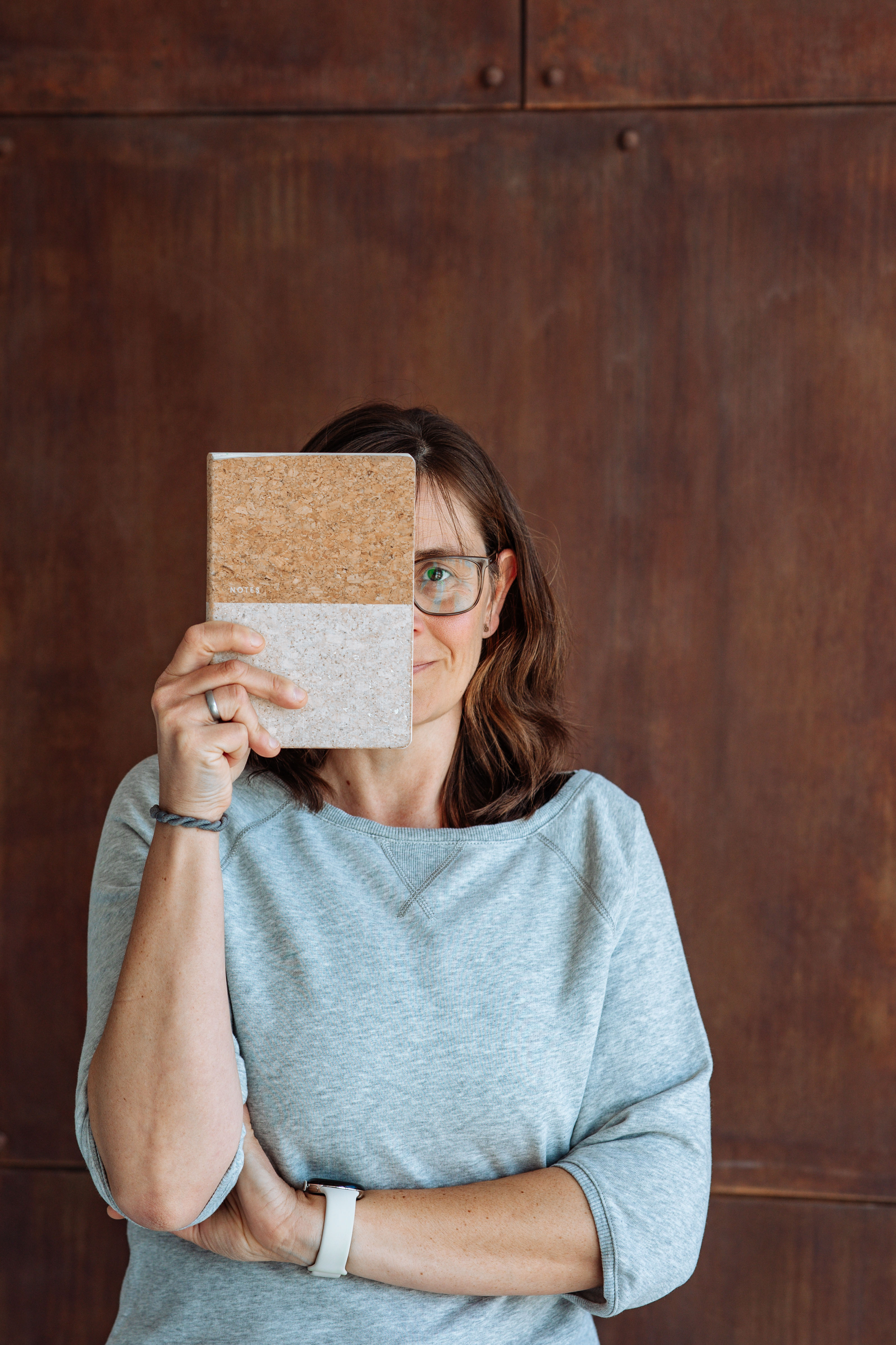 Frau hält sich Notizbuch vor das Gesicht.