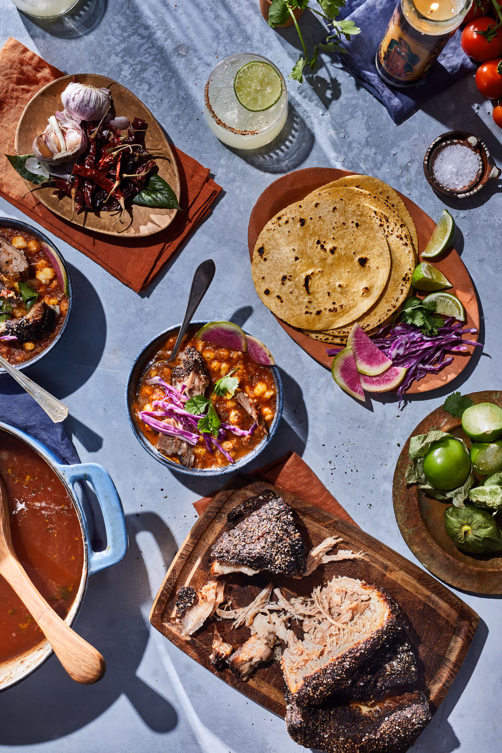 An over head photograph of a Pozole with charred tortillas and watermelon radishes. The table top is littered with other dishes and flavor cues. Photo by Christi Chambers.