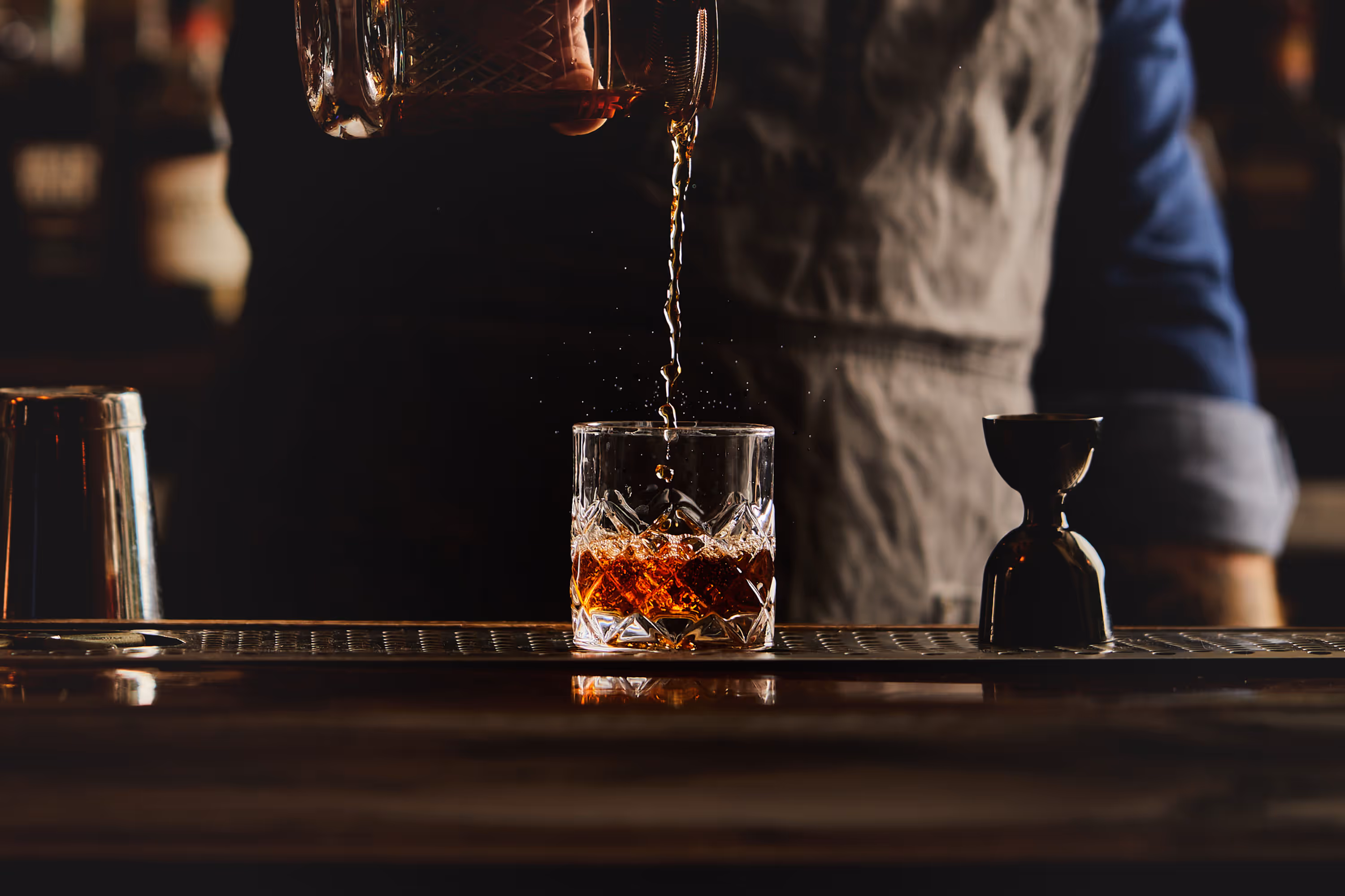 A low-key action shot of a bartender pouring a whiskey cocktail into a rocks glass. Photograph by Christi Chambers.