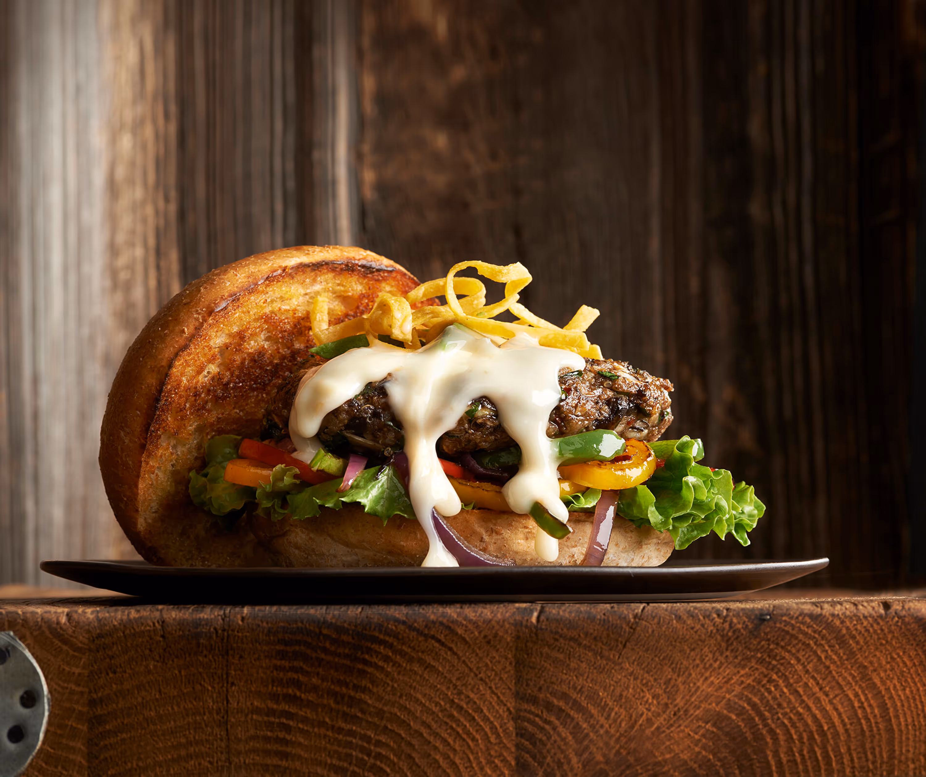 A Photograph of a thick hamburger on a wooden surfaces, covered in Chef-mate Cheese Sauce. Shot by Ralph Smith.