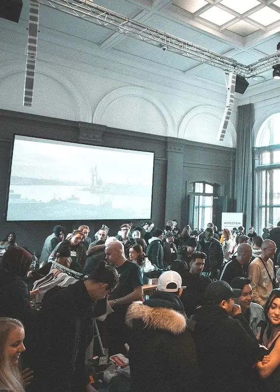 A group of people milling about in a warehouse style room at a party
