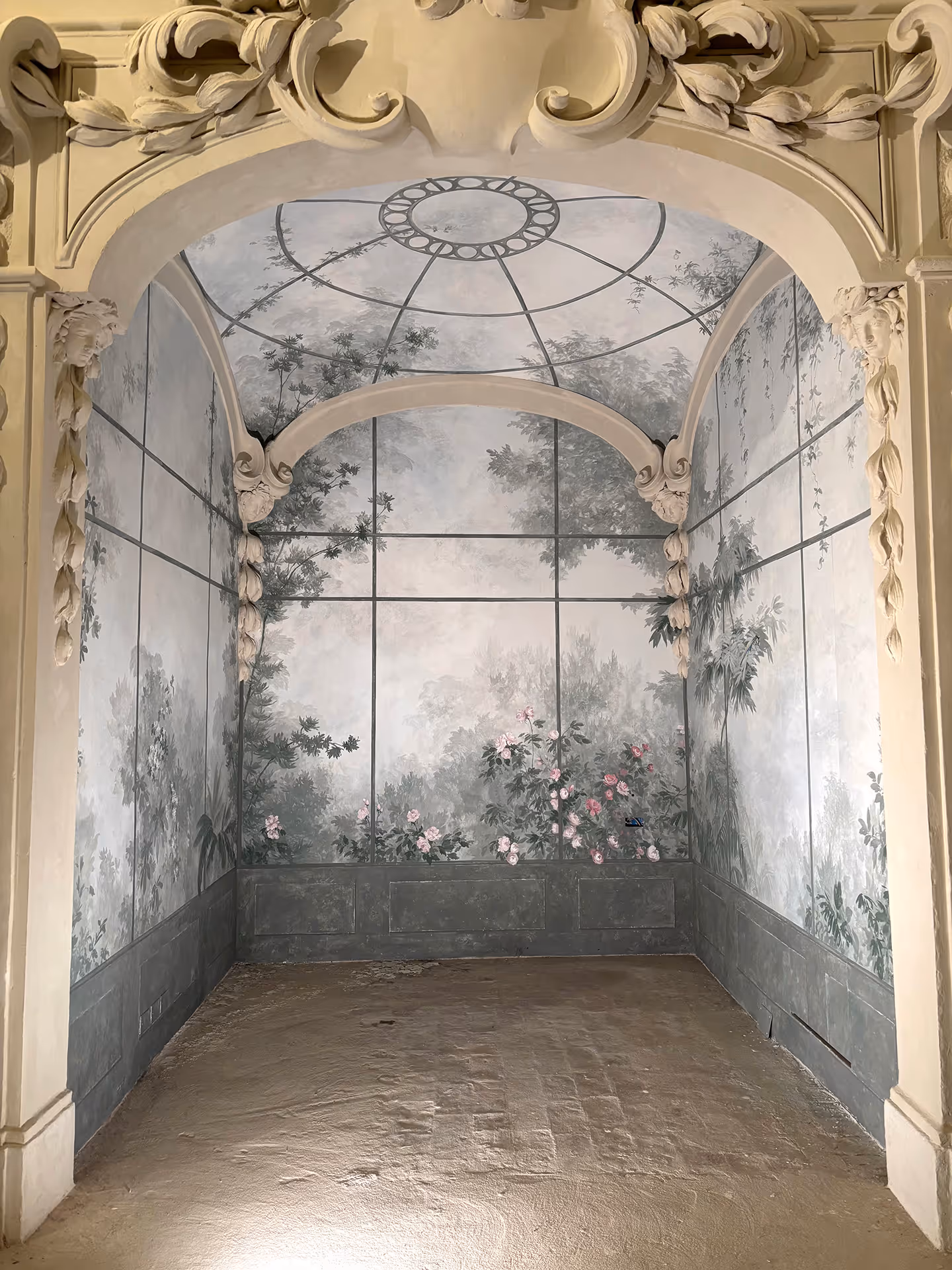 Trompe-l’œil mural by a London mural painter featuring a curved dome ceiling with classical corner ornaments and faces, walls painted to resemble a misty forest with shrubs, trees, and roses in the foreground.