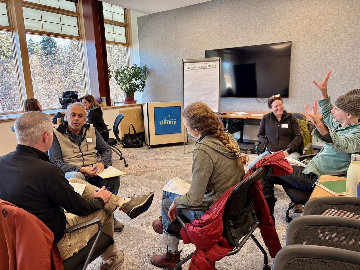 A group standing together with Bozeman facilitator and coach Emily Stifler Wolfe, at one of her free monthly facilitated sessions on leadership and collaboration at Bozeman Public Library. 