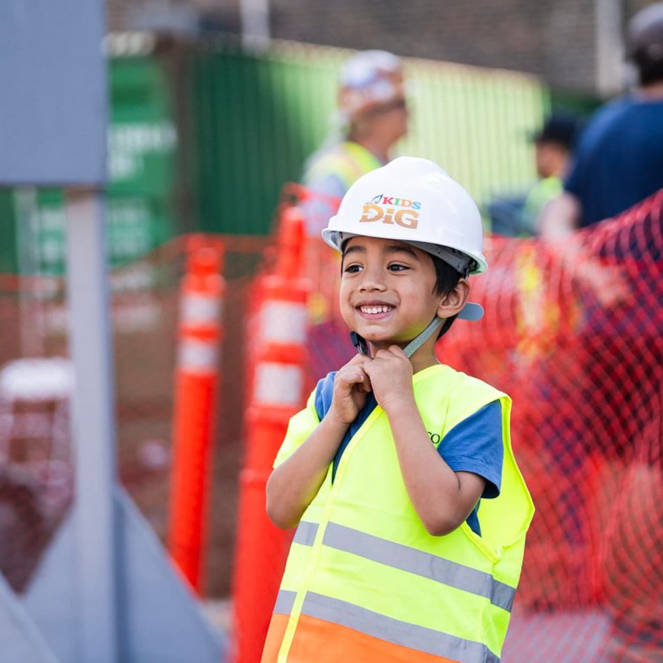 Young boy in a hard hat and safety vest smiling at the Clayco Kids Dig construction-themed event.
