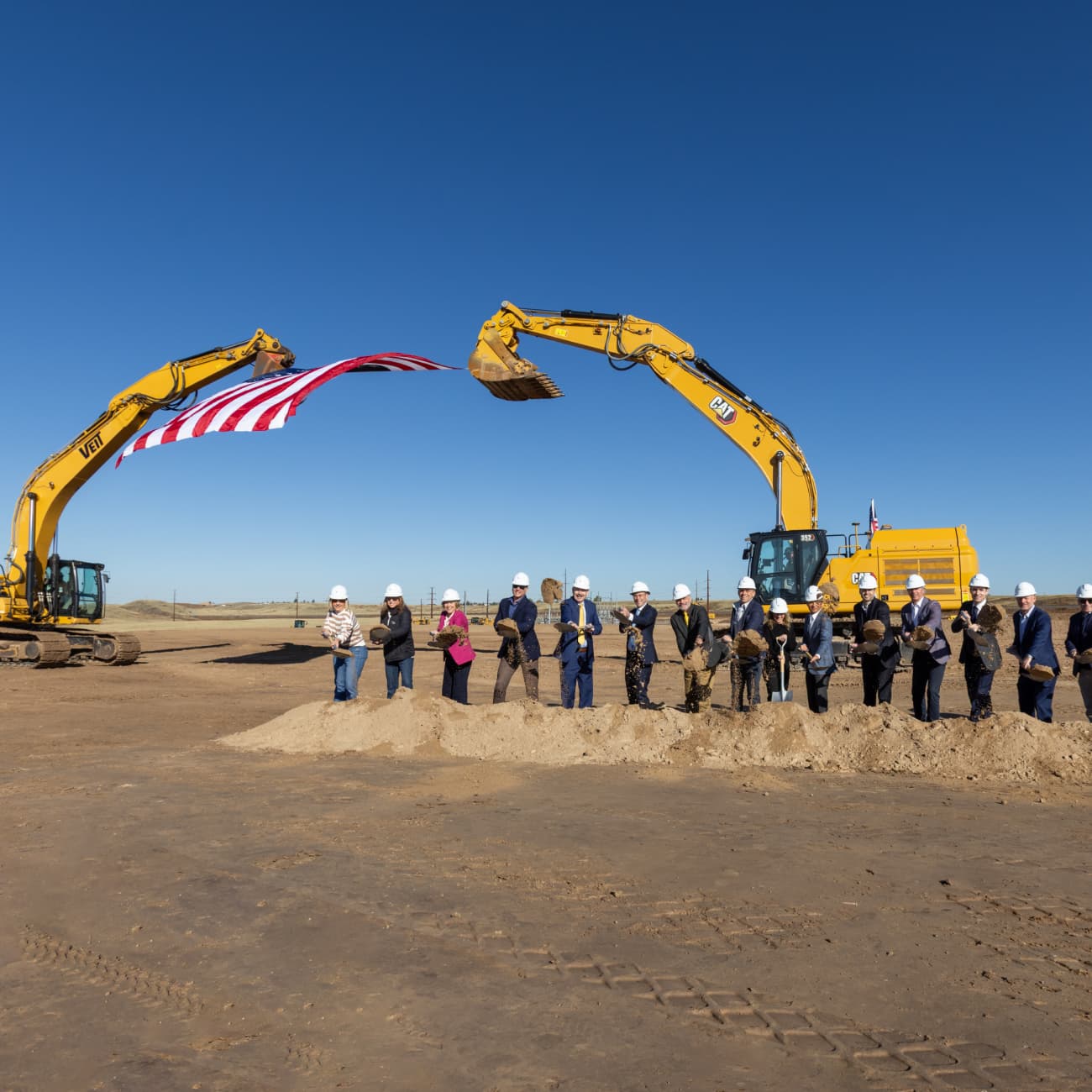 Leaders from Clayco, Related Digital, and local officials participate in the groundbreaking ceremony for a 115-acre data center campus in Cheyenne, Wyoming, standing under two excavators holding an American flag.