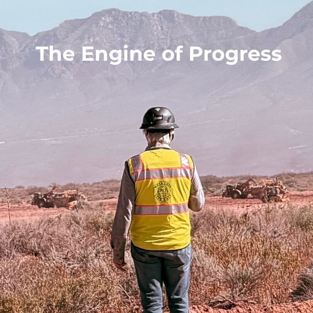 Construction worker in a yellow safety vest and hard hat standing on a desert job site, facing large equipment and distant mountains, with the text “Why AI? Why Now?” symbolizing the intersection of technology, industry, and the next era of innovation.