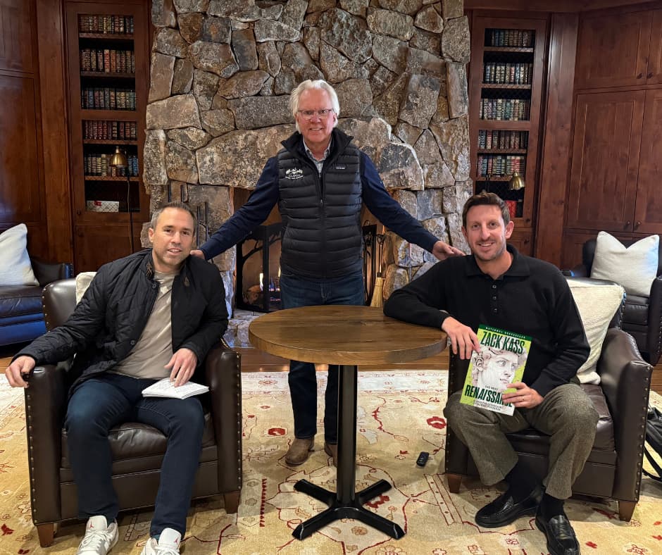 Bob Clark with Zach Kass and Shawn Clark during a relaxed conversation in a lodge-style room, with Kass holding his new book on ethical AI.