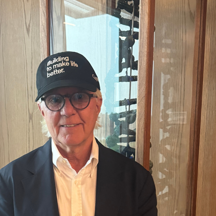 man in a black hat that says building to make life better standing in front of a dna sculpture