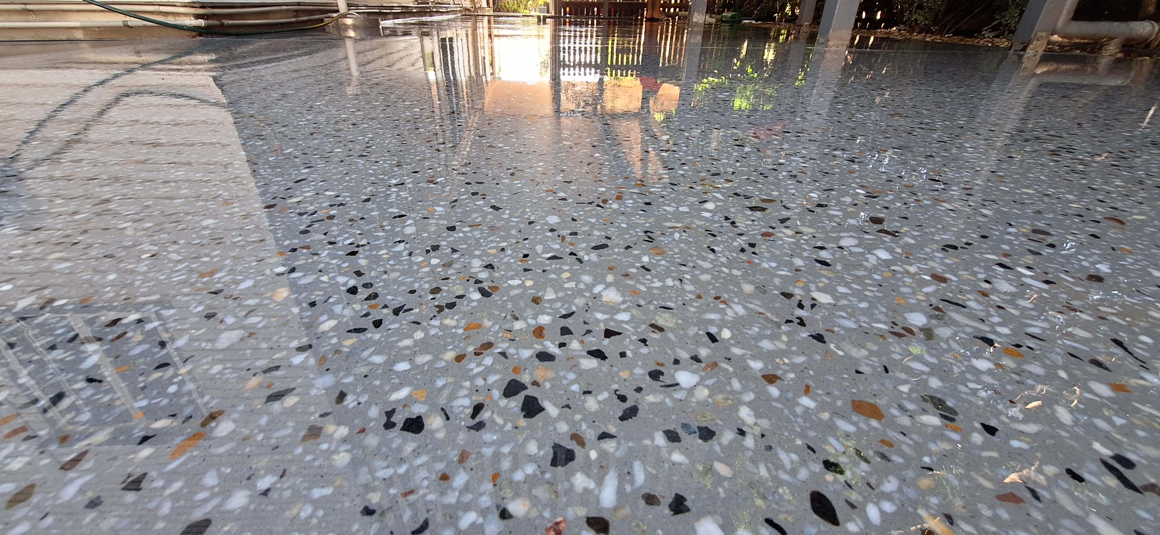 Polished terrazzo floor with multicolored stone chips reflecting a building and outdoor surroundings.