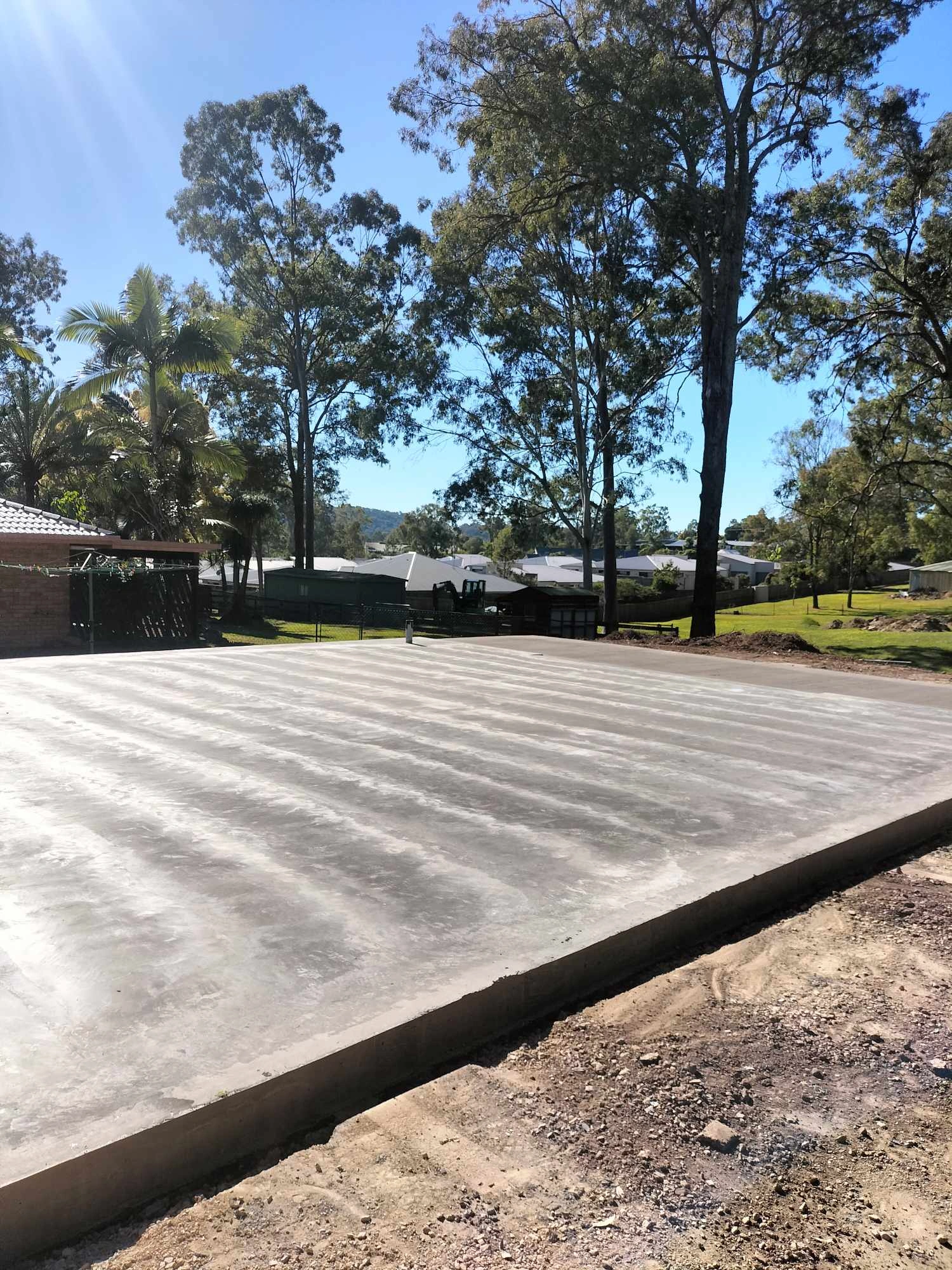 Freshly poured large smooth concrete slab in a sunny outdoor area with trees and houses in the background.