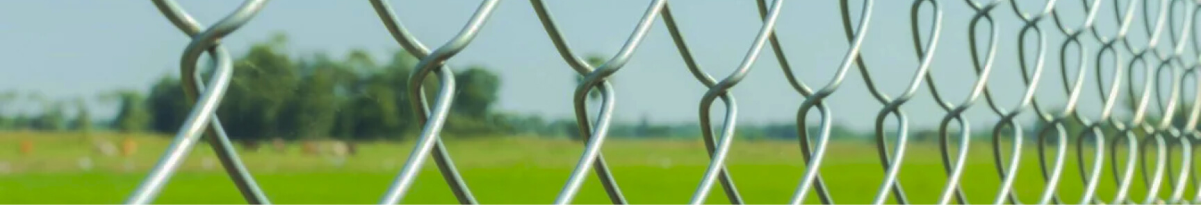 A close-up of a chain link fence in front of a grassy field.