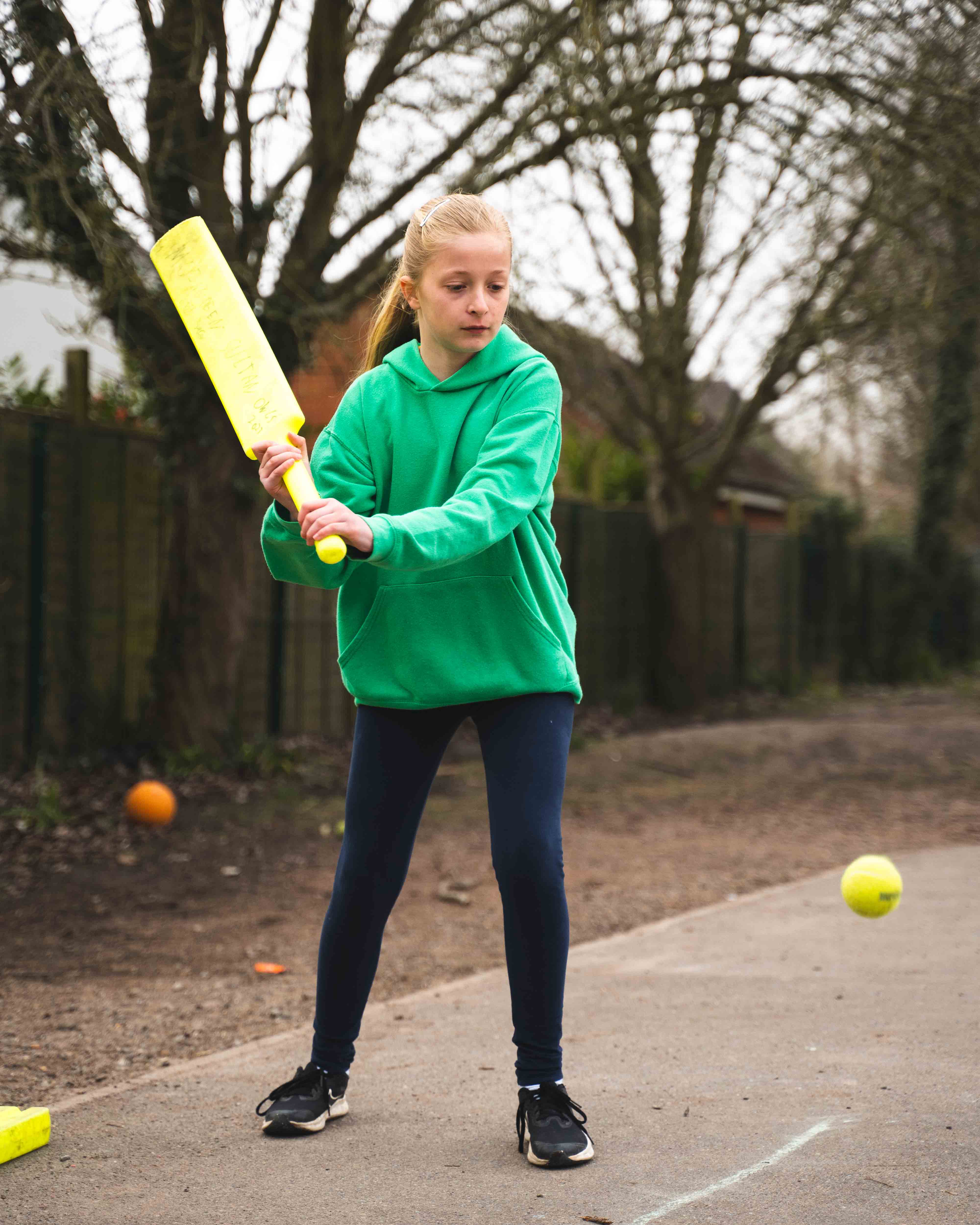 A girl playing cricket in a school playground ready to hit a tennis ball. 