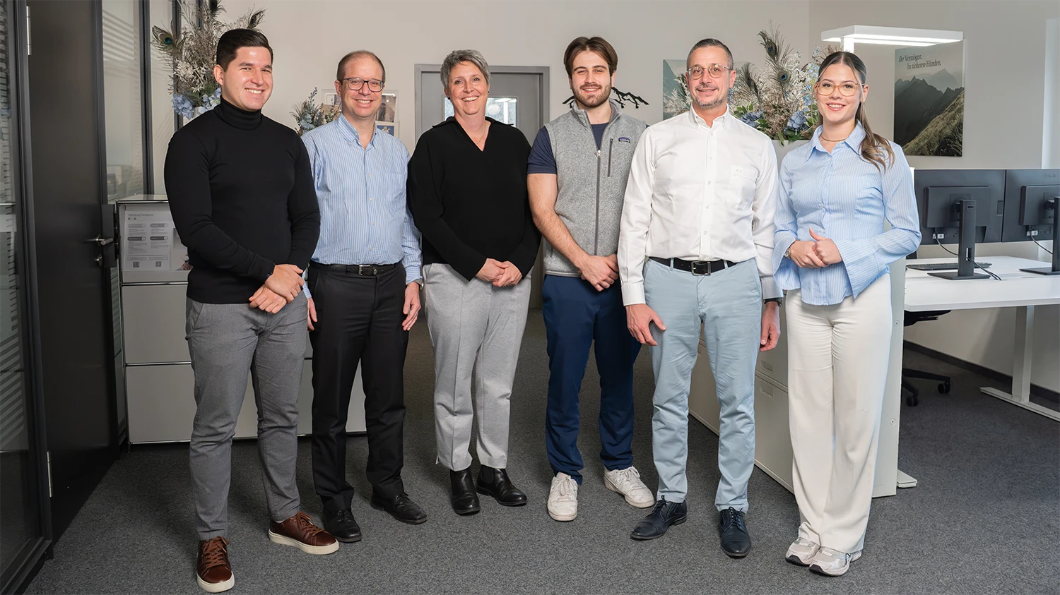 Sechs Personen stehen in einem Büro, lächeln und schauen in die Kamera.