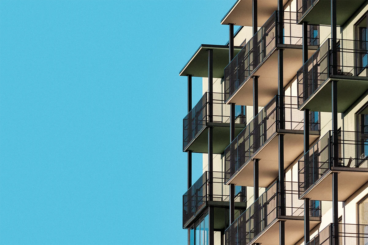 Moderner Wohnblock mit mehreren Balkonen vor klarem blauem Himmel.