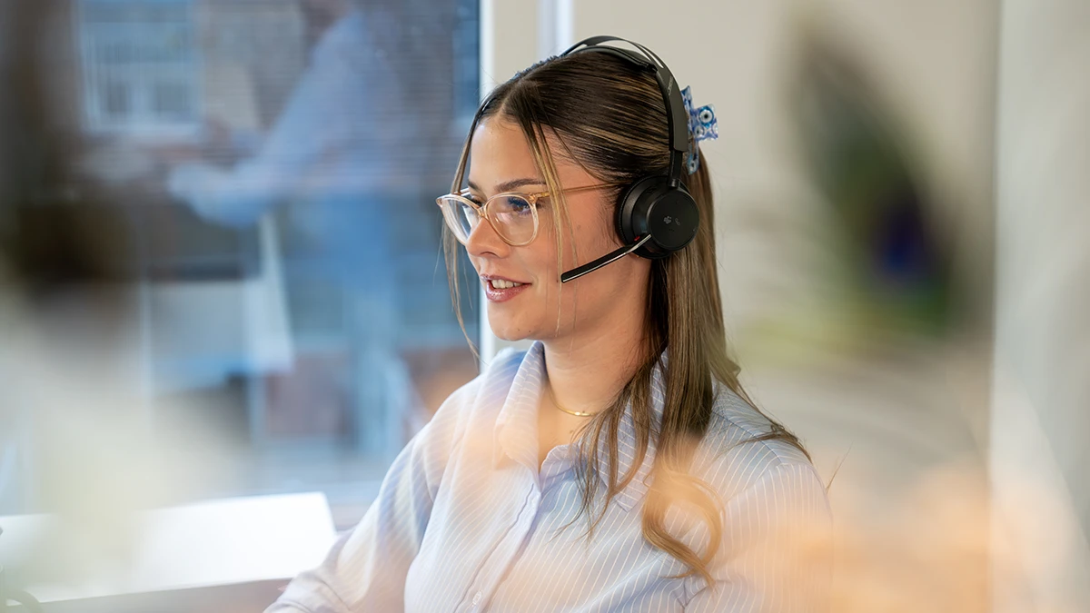 Frau mit Brille und Headset arbeitet an einem Computer in einem modernen Büro.