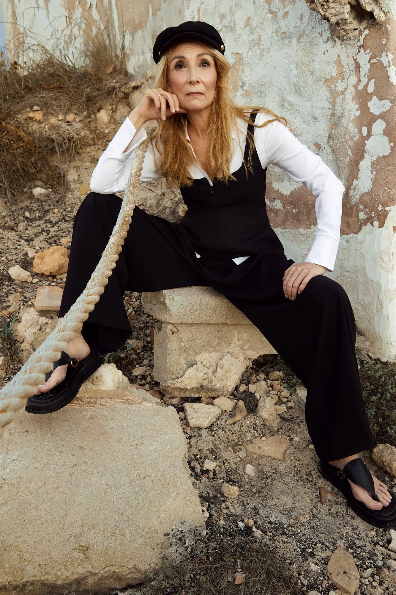 Eine Frau in grünem Blazer und weißen Hosen sitzt lässig auf einem Stuhl