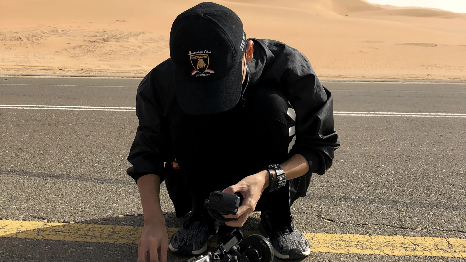 Crewmitglied mit Kamera bei einem Videodreh an einer Wüstenstraße, Gesicht verdeckt