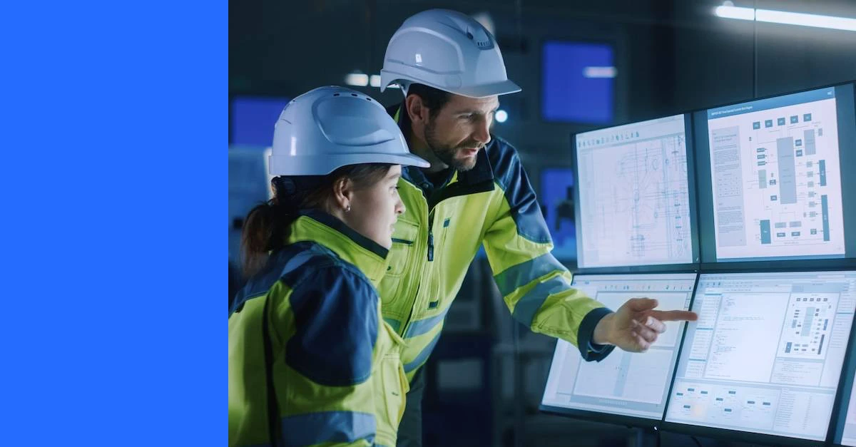 Modern factory project manager talks to engineer, she points at computer screens showing industrial electronics design blueprints