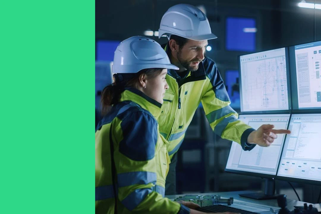 Modern factory project manager talks to engineer, she points at computer screens showing industrial electronics design blueprints