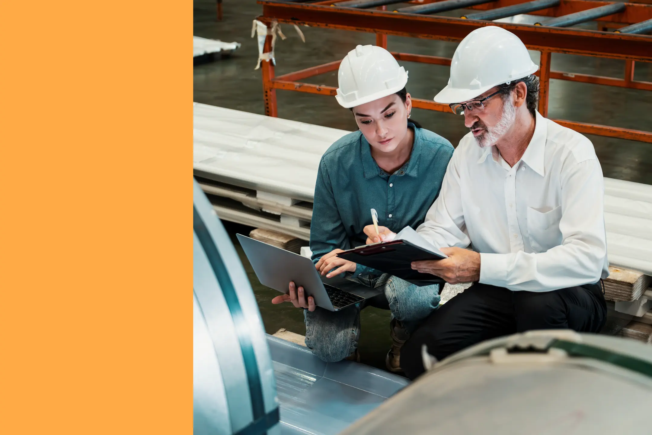 Two industrial maintenance workers are kneeling by production equipment in a manufacturing plant. One is showing the other something on a mobile device, while the second worker has a laptop.