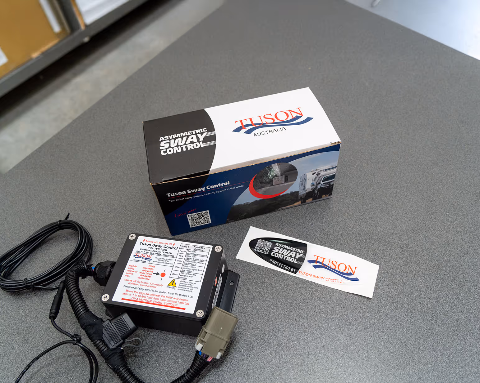 Tuson Sway Control device with wiring harness, product box, and decal on a gray surface.