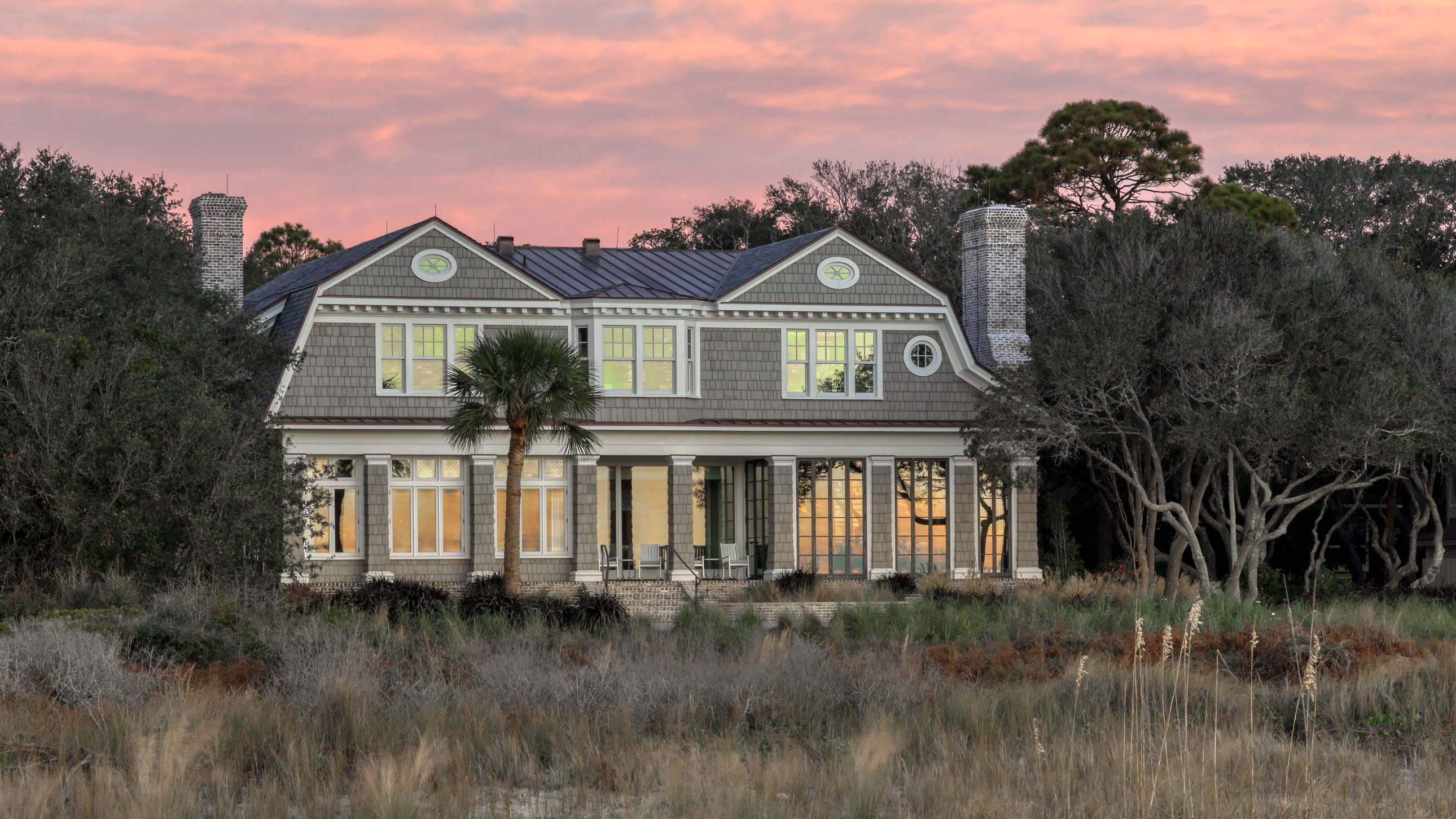A design detail shot of wicker porch furniture with coastal throw pillows and a tray of sun-bleached seashells