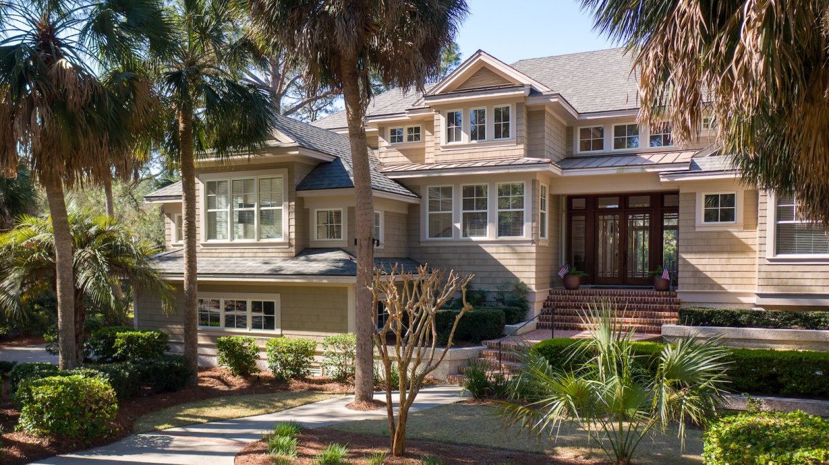 A design detail shot of wicker porch furniture with coastal throw pillows and a tray of sun-bleached seashells
