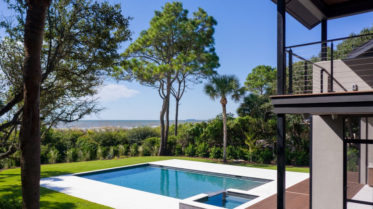 A design detail shot of wicker porch furniture with coastal throw pillows and a tray of sun-bleached seashells