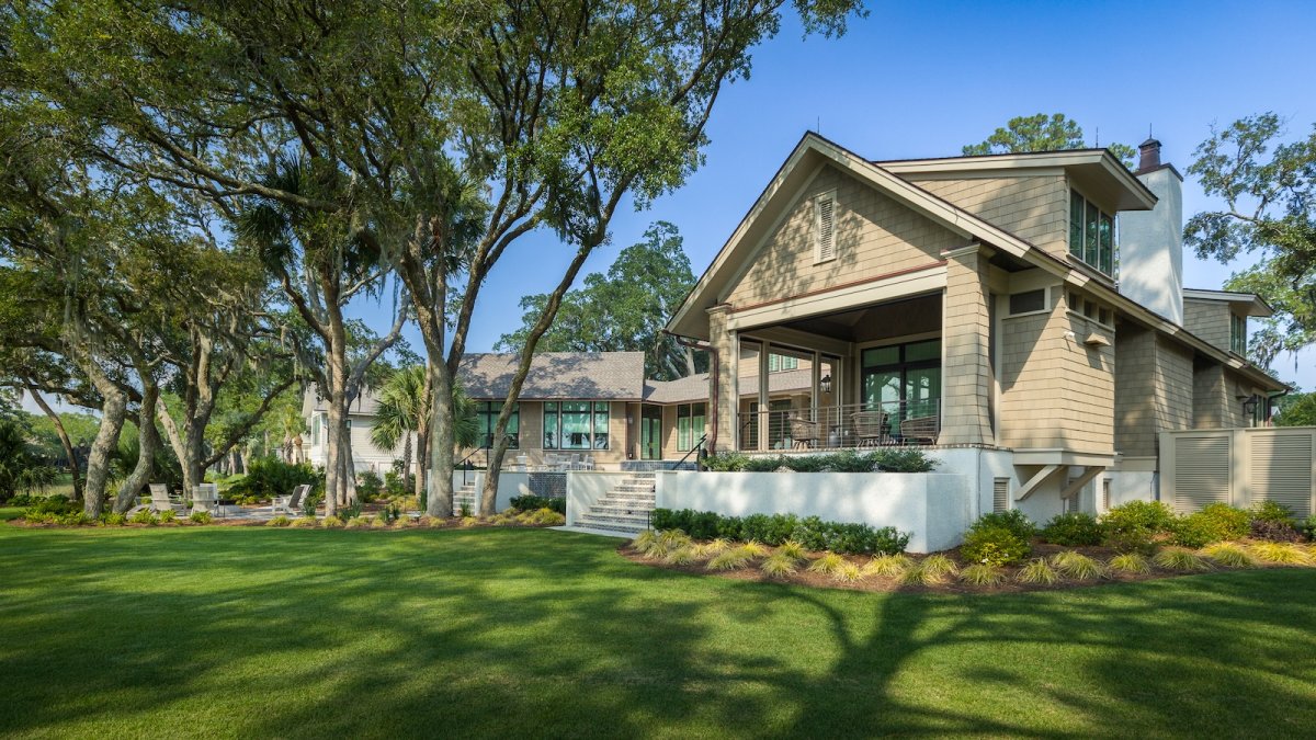 A design detail shot of wicker porch furniture with coastal throw pillows and a tray of sun-bleached seashells
