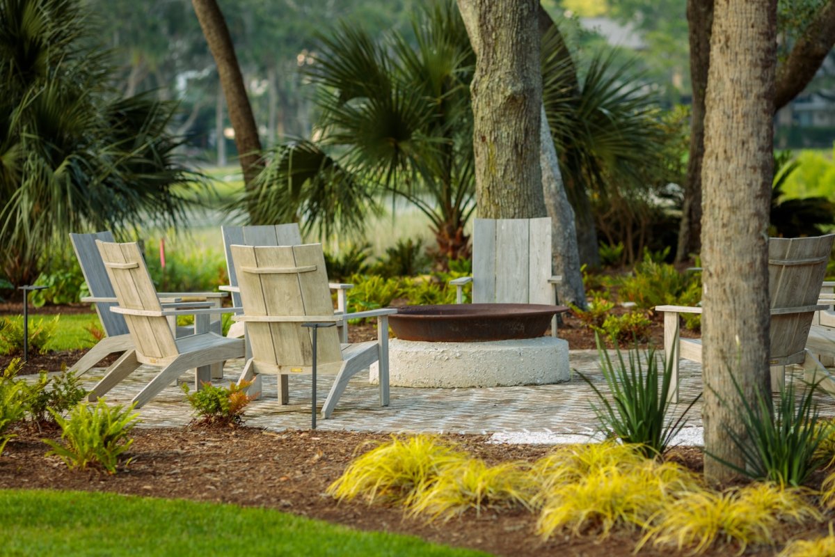 A design detail shot of wicker porch furniture with coastal throw pillows and a tray of sun-bleached seashells