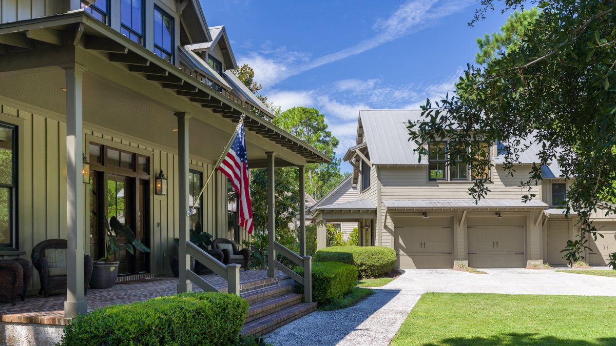 A design detail shot of wicker porch furniture with coastal throw pillows and a tray of sun-bleached seashells
