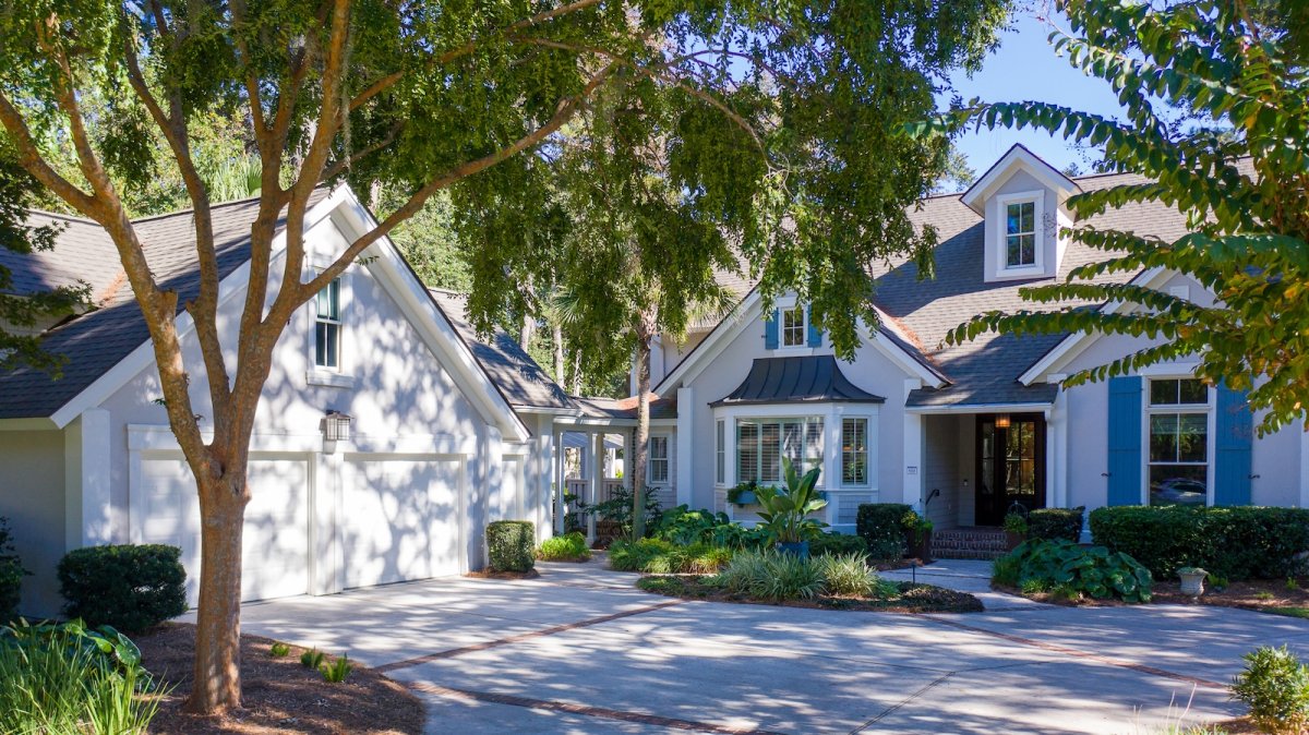 A design detail shot of wicker porch furniture with coastal throw pillows and a tray of sun-bleached seashells