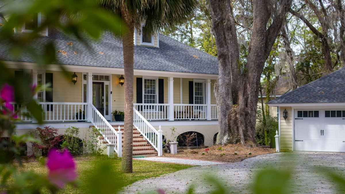 A design detail shot of wicker porch furniture with coastal throw pillows and a tray of sun-bleached seashells
