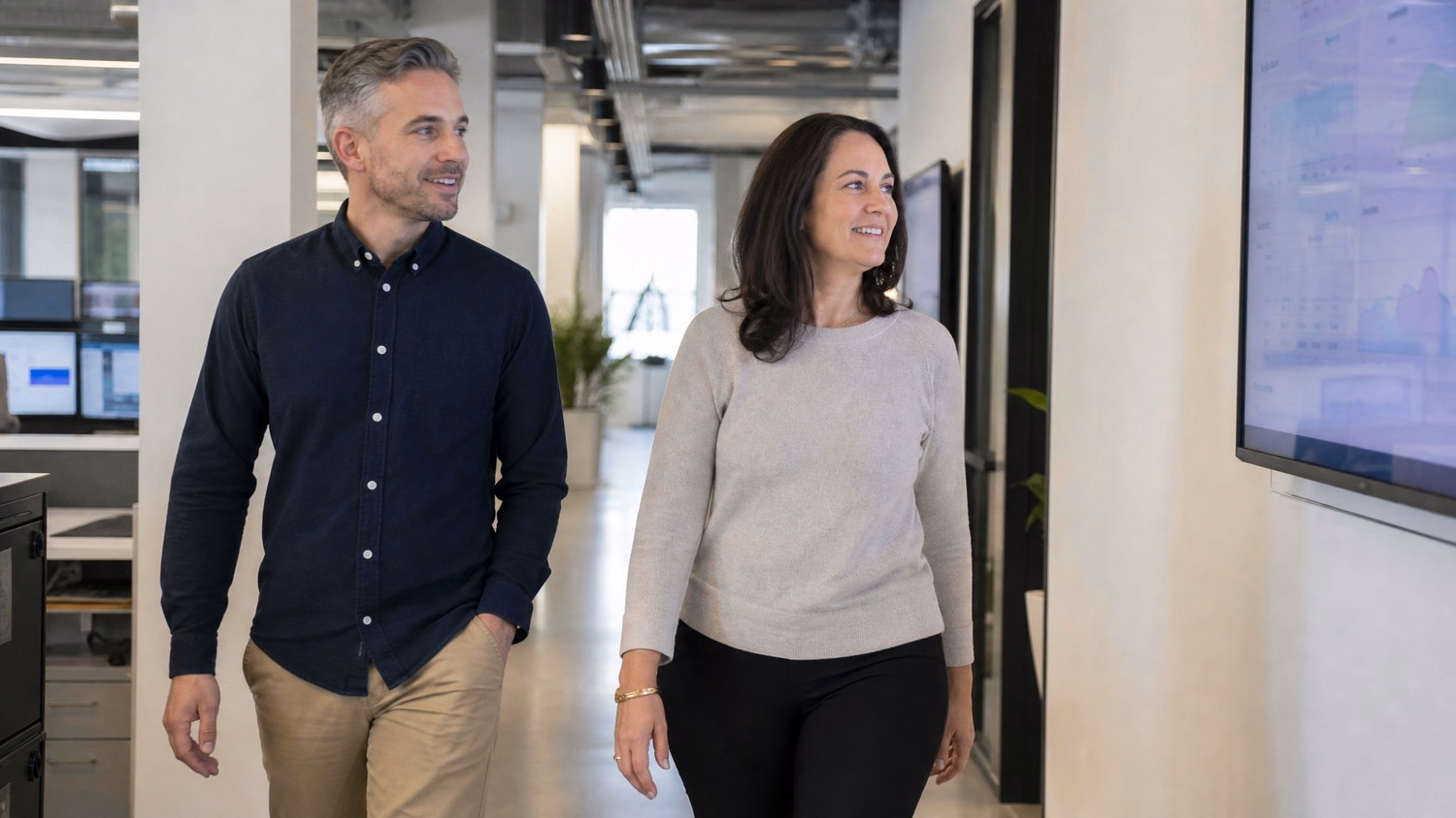 Man and woman walk through office, look at monitor 61 chars