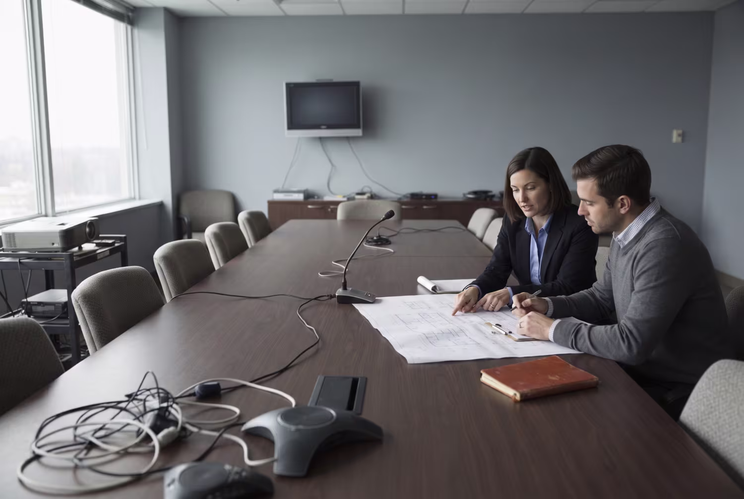 Professionals discussing blueprints in a mismatched conference room AV setup