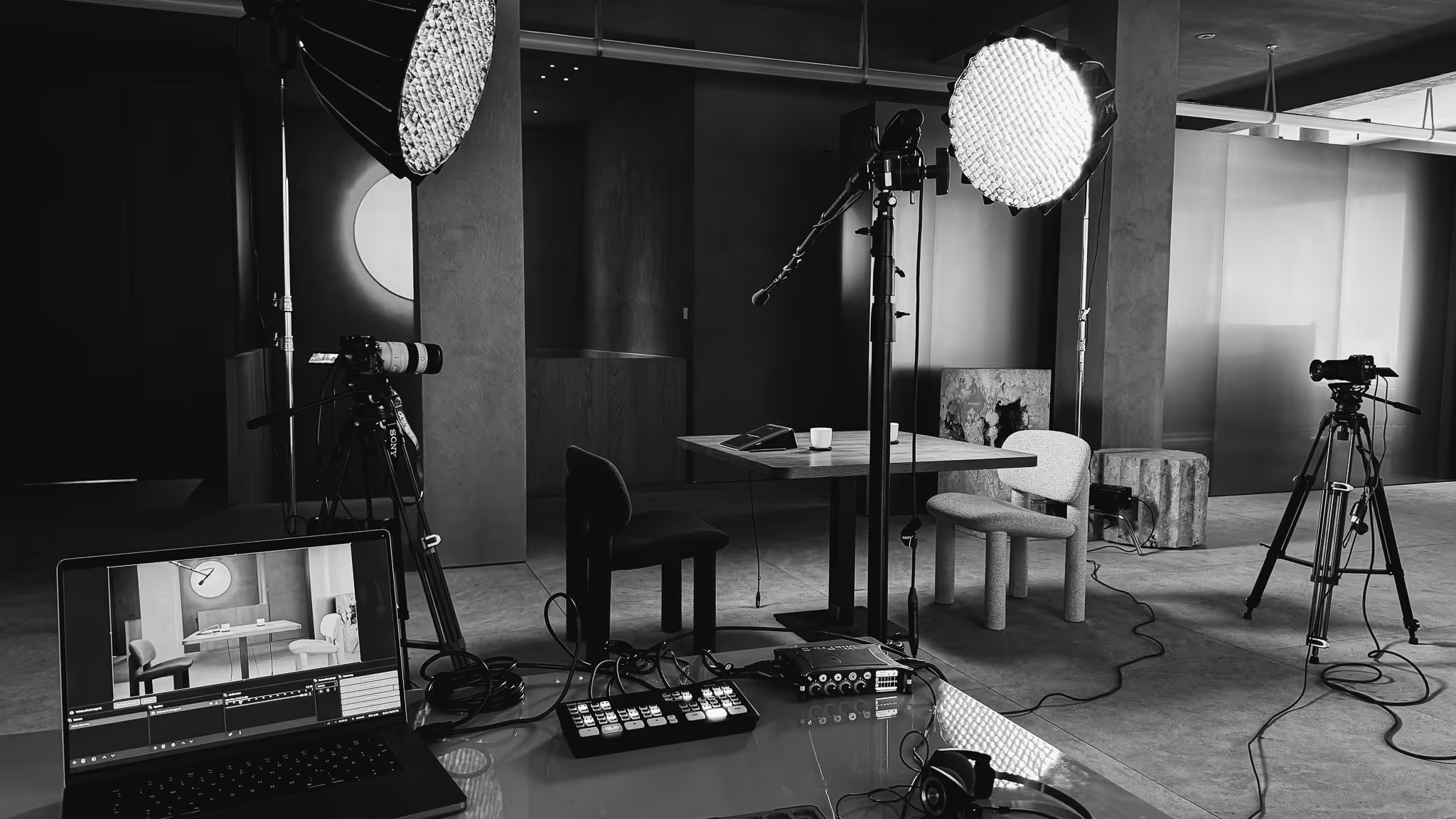 Professional studio setup with cameras on tripods, large softbox lights, microphone, and a table with two chairs.