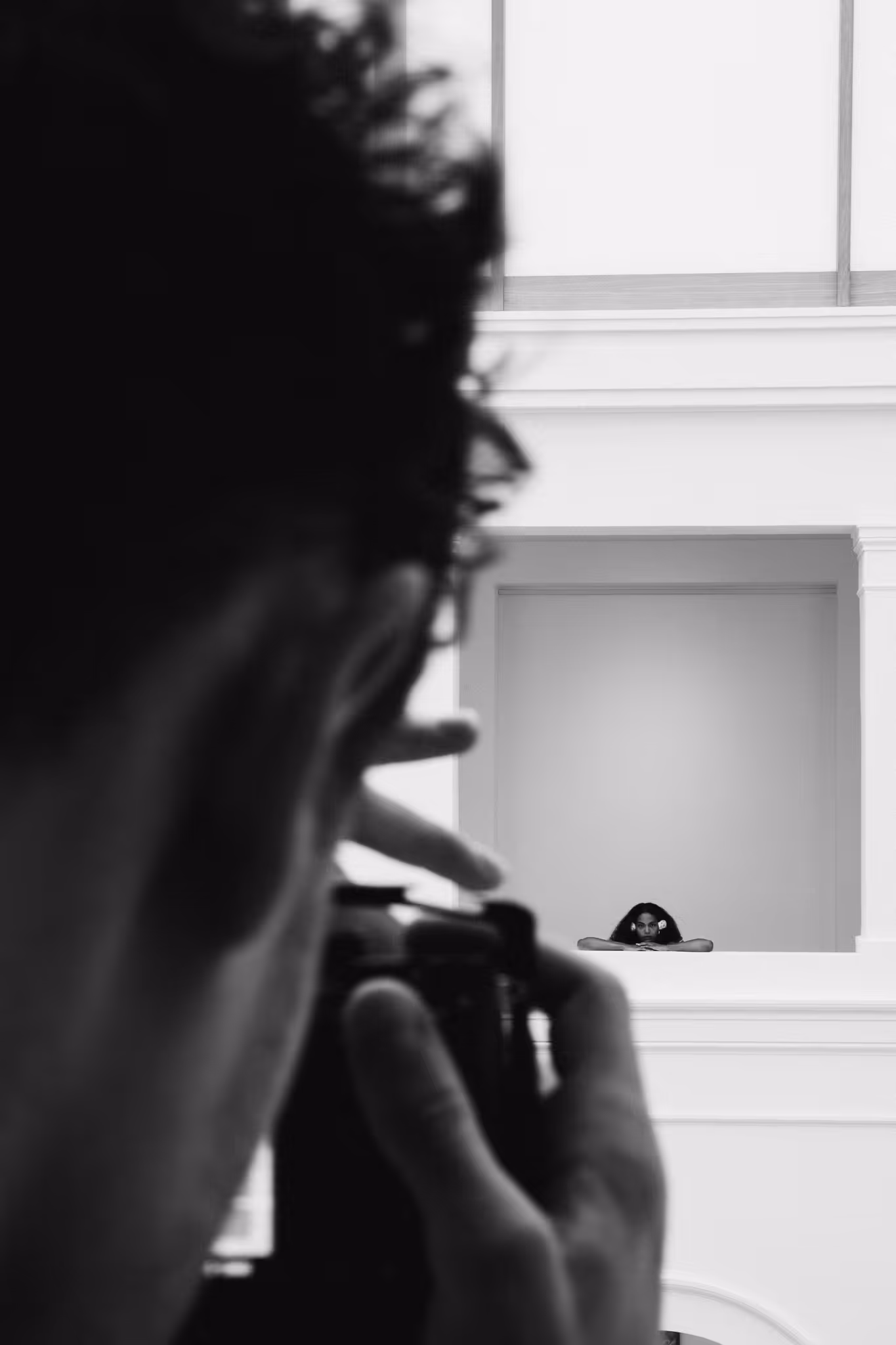 Photographer taking a photo of a woman with a flower in her hair leaning on a white balcony.