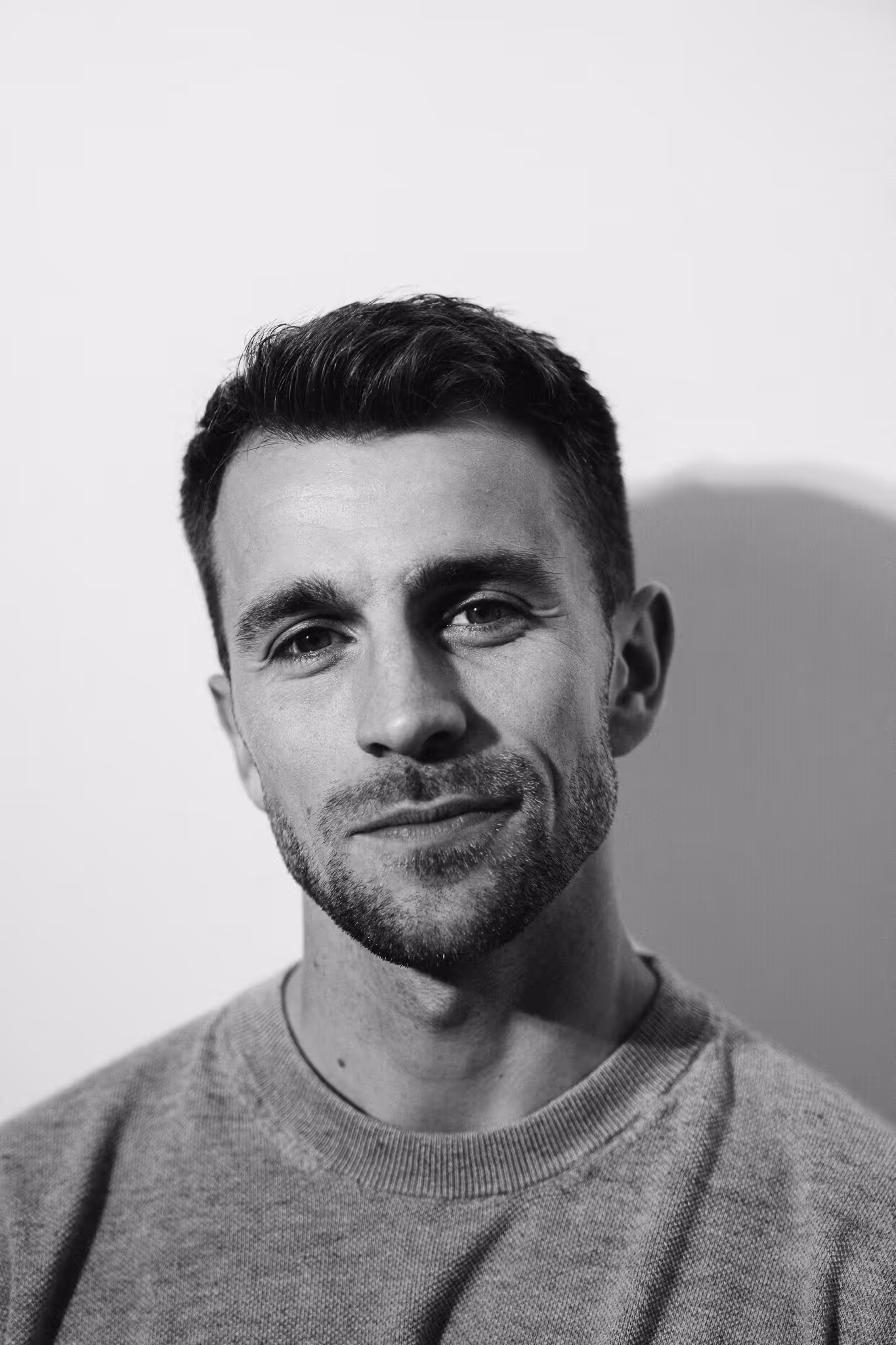 Black and white close-up portrait of a smiling man with short hair and a beard wearing a sweater.