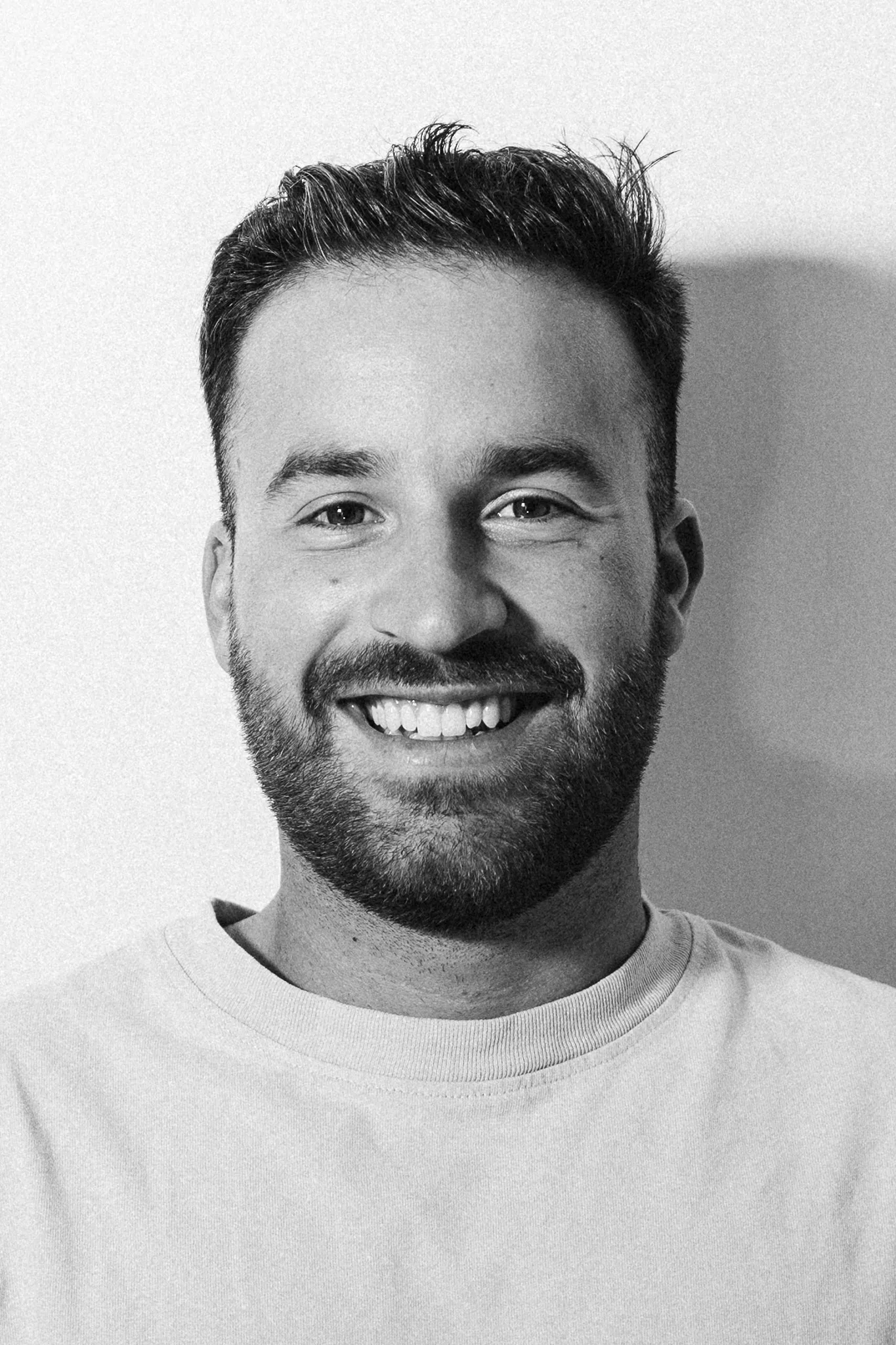 Black and white portrait of a smiling bearded man with short hair wearing a crew neck shirt.