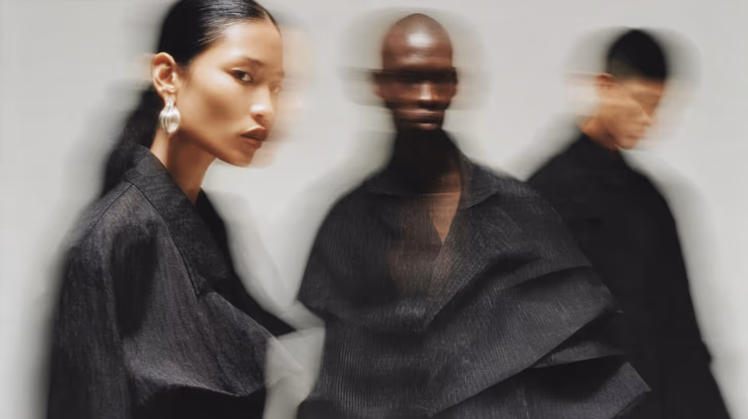 Three fashion models wearing dark, textured clothing with motion blur effect on a light gray background.
