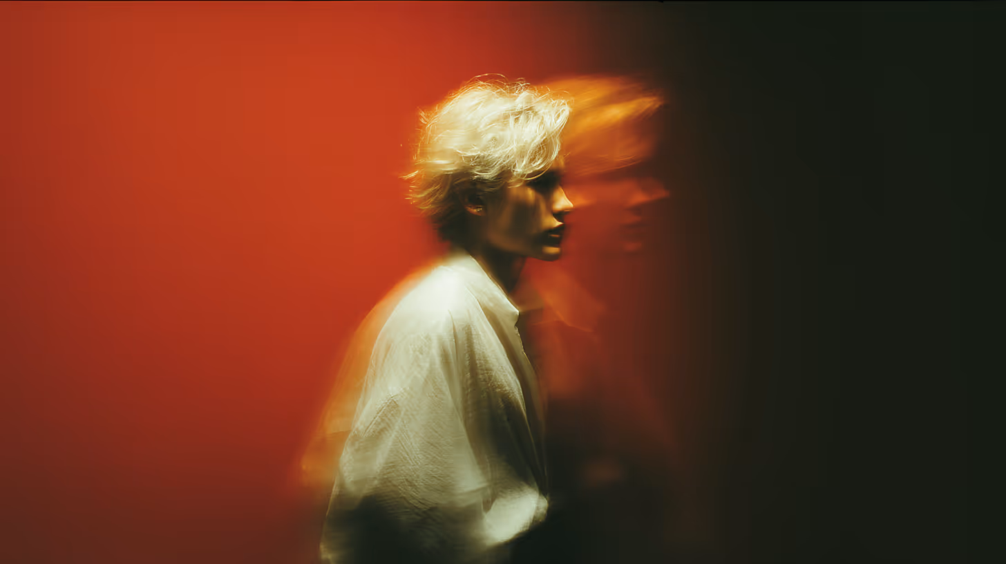 Blonde person in white shirt with blurred double exposure effect against a red and black background.